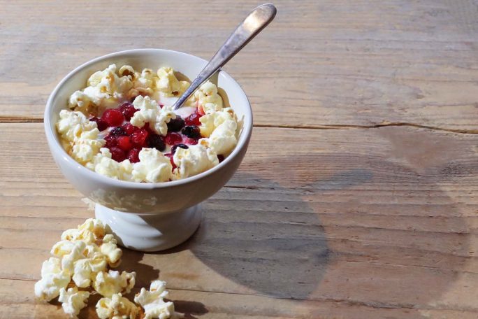 Schüssel mit Popcorn und einer Topping aus roten Beeren auf einem Holztisch.